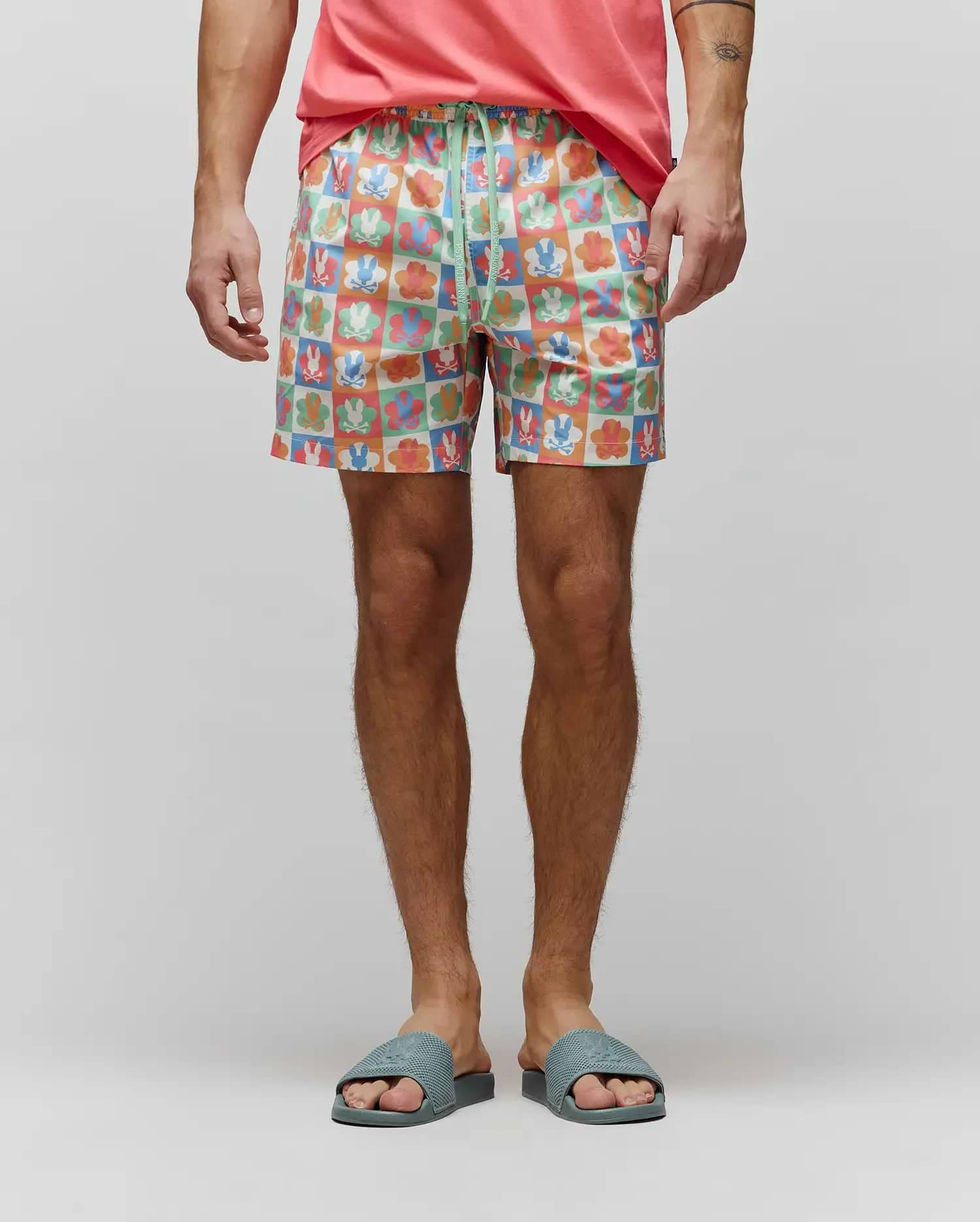 Mens Aiden Swim Trunk in a vibrant multi-color checkered print featuring Psycho Bunny skull logos and flower graphics, with a green drawstring displaying the brand name. Relaxed fit, smooth fabric. (1)