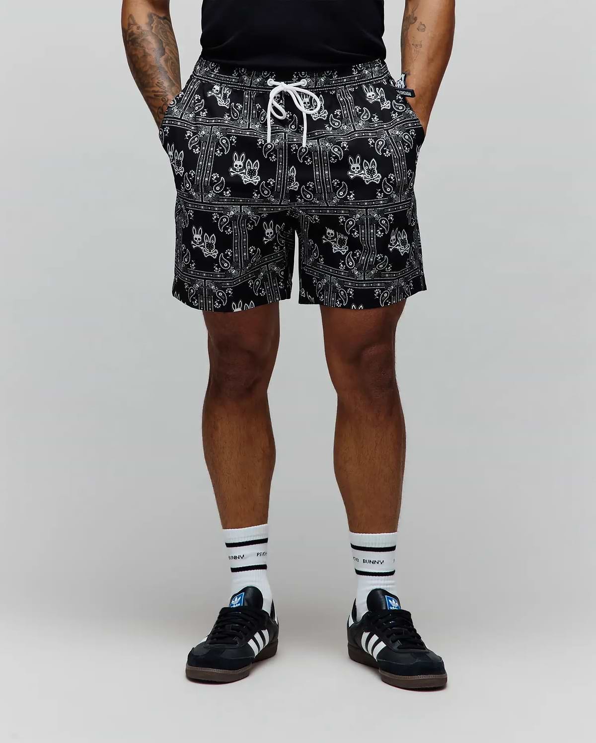 Mens Luke Swim Trunk in black, featuring an all-over white bandana paisley print with integrated Psycho Bunny skull logos, an elastic waistband, and a white drawstring for a relaxed fit.