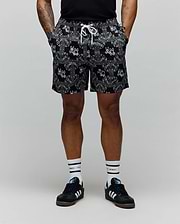 Mens Luke Swim Trunk in black, featuring an all-over white bandana paisley print with integrated Psycho Bunny skull logos, an elastic waistband, and a white drawstring for a relaxed fit.