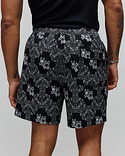 Mens Luke Swim Trunk in black with a white all-over bandana paisley print featuring repeated Psycho Bunny skull logos, a relaxed fit, and smooth quick-dry fabric.