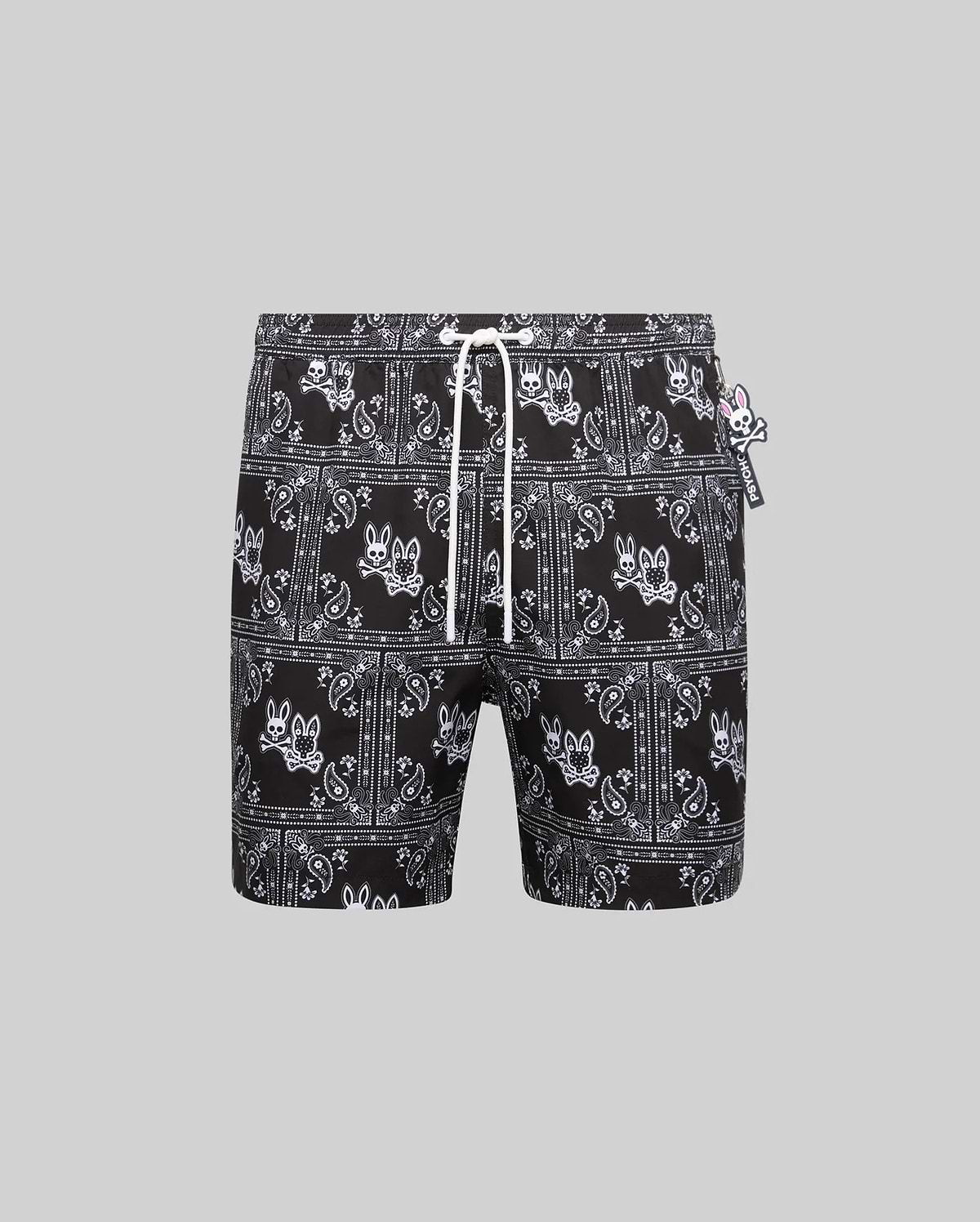 Mens Luke Swim Trunk in black with an all-over white bandana paisley print featuring the iconic Psycho Bunny skull logo, complete with a white drawstring and small Psycho Bunny tag, offering a classic fit in smooth, quick-dry fabric.