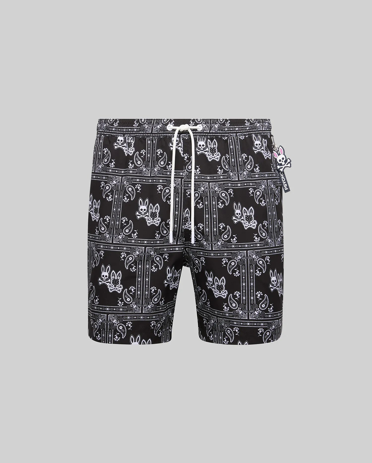 Mens Luke Swim Trunk in black with an all-over white bandana paisley print featuring the iconic Psycho Bunny skull logo, complete with a white drawstring and small Psycho Bunny tag, offering a classic fit in smooth, quick-dry fabric.