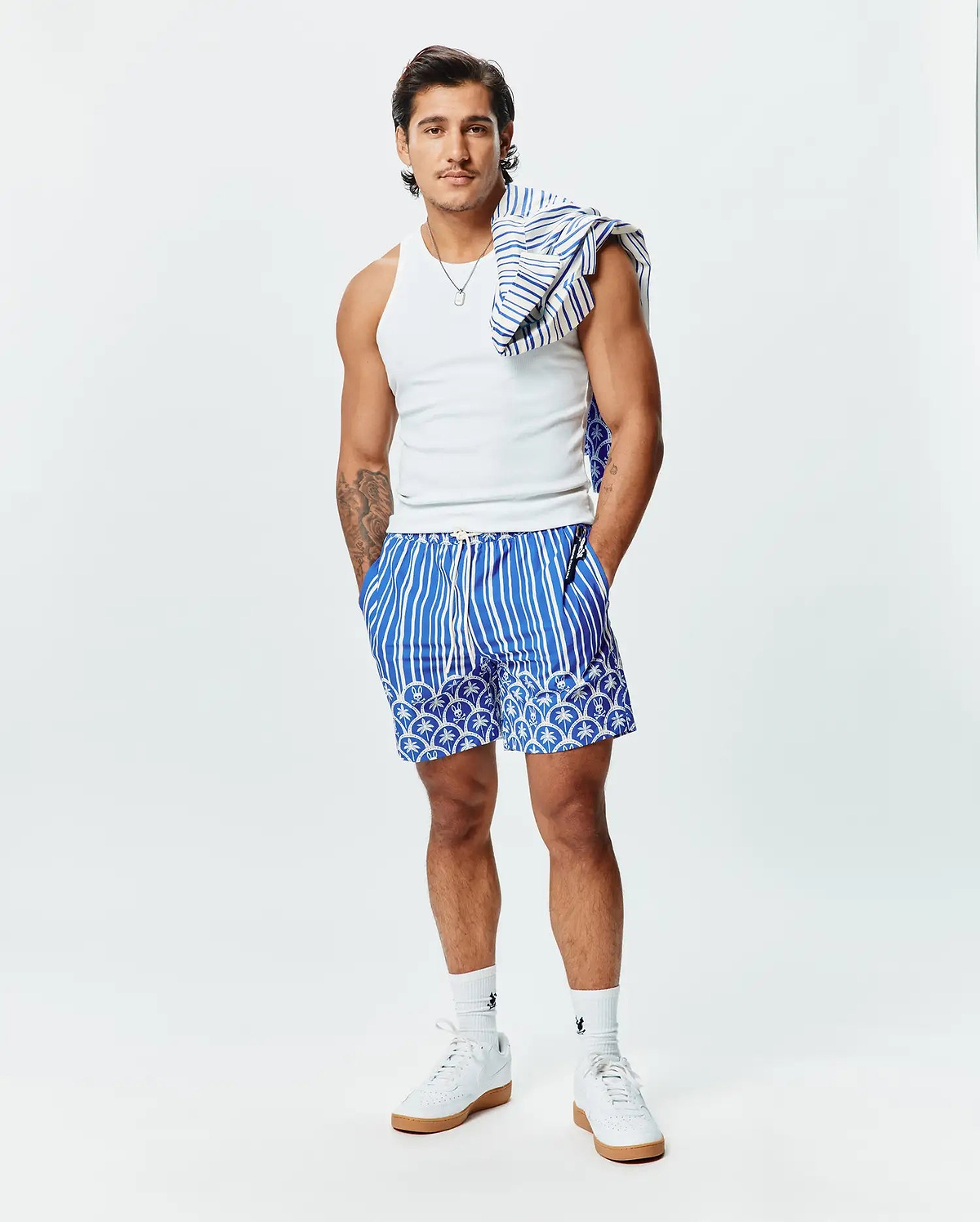 Mens Brad Swim Trunk in royal blue with bold white vertical stripes, featuring a unique lower pattern of white Psycho Bunny skull logos and palm trees, with a small logo on the back pocket zipper pull.