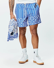 Mens Brad Swim Trunk in blue with white vertical stripes, transitioning to a scalloped pattern featuring palm trees and small Psycho Bunny skull logos. Relaxed fit, smooth fabric.