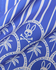 Mens Brad Swim Trunk in royal blue with white vertical stripes, an all-over print featuring white palm trees, and the iconic Psycho Bunny skull logo within decorative circles on a smooth woven fabric.