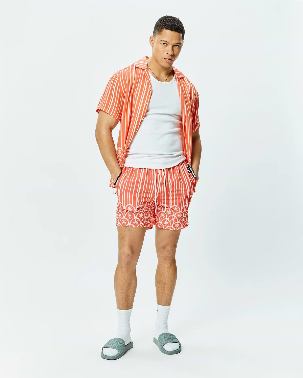 Coral striped short-sleeve button-up shirt with sleeve logo, white crew neck t-shirt, and Mens Brad Swim Trunk featuring matching stripes, palm tree, and bunny skull pattern with Psycho Bunny drawstring.