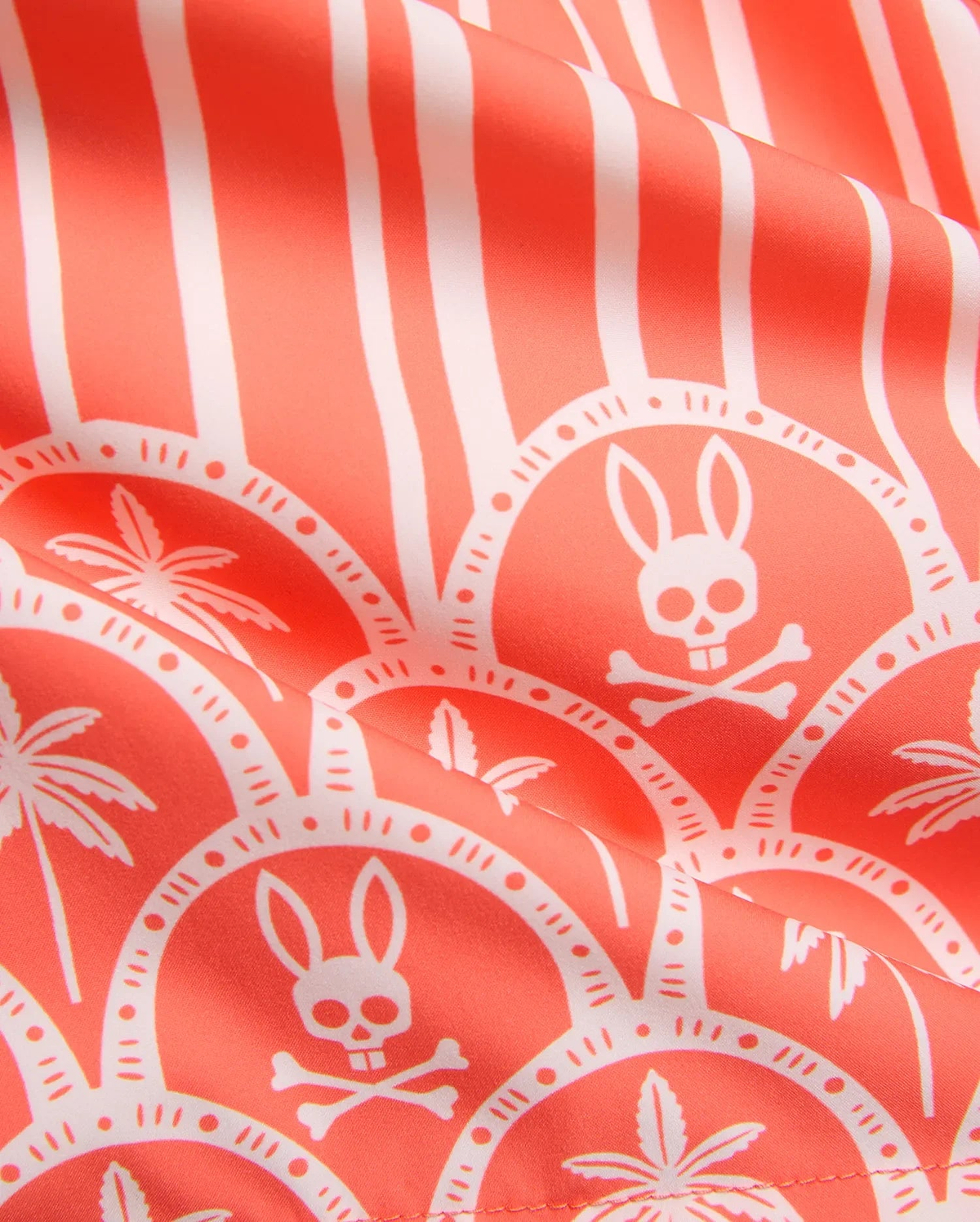MENS BRAD SWIM TRUNK in vibrant coral with an all-over white print featuring vertical stripes, scalloped patterns, the iconic Psycho Bunny skull logo, and tropical palm trees on smooth fabric.