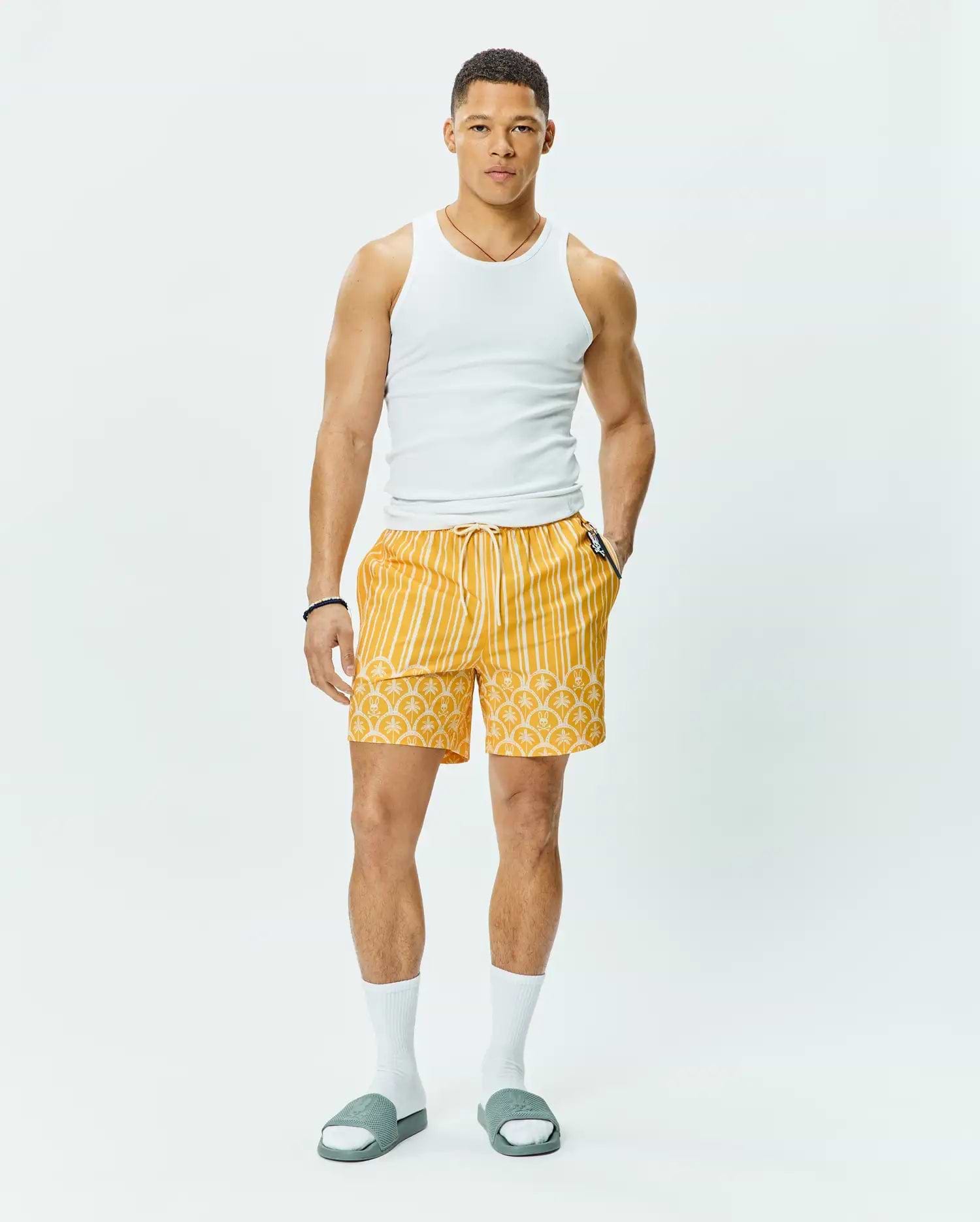 Mens Brad Swim Trunk, vibrant yellow with white vertical stripes on top, transitioning to an all-over Psycho Bunny skull logo pattern on the bottom, featuring a relaxed fit, smooth quick-dry fabric, and a white drawstring waist.