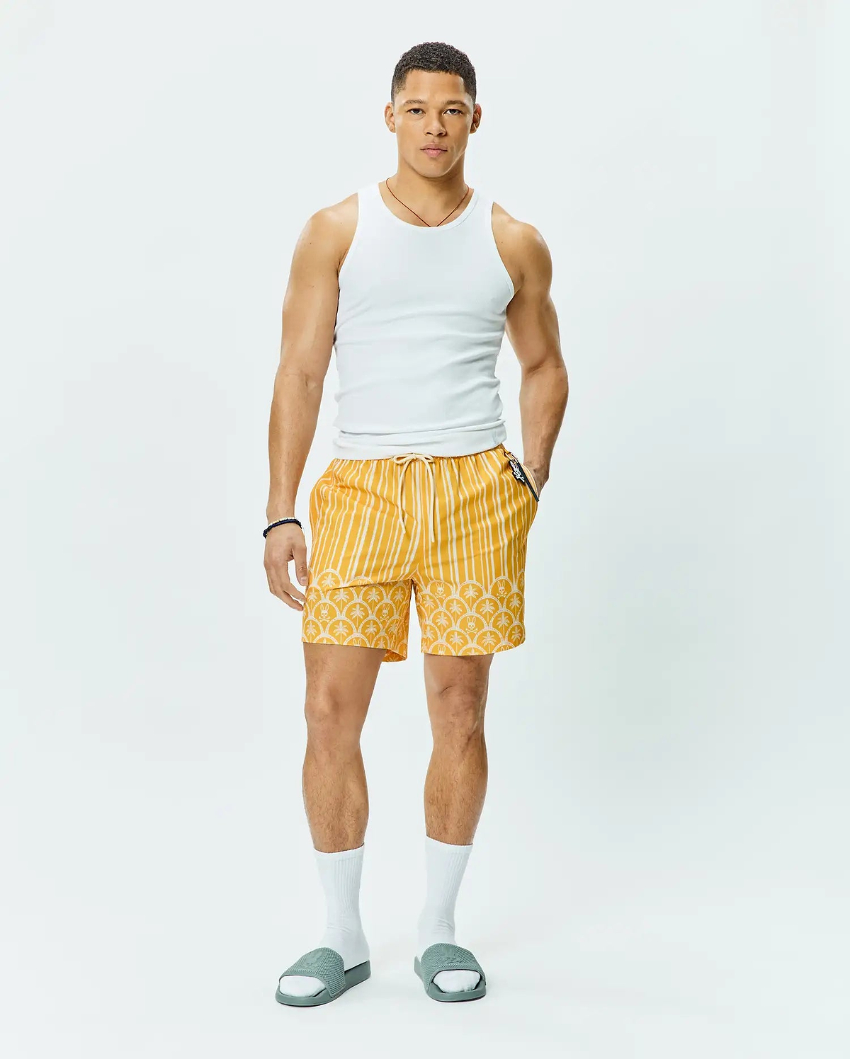 Mens Brad Swim Trunk, vibrant yellow with white vertical stripes on top, transitioning to an all-over Psycho Bunny skull logo pattern on the bottom, featuring a relaxed fit, smooth quick-dry fabric, and a white drawstring waist.