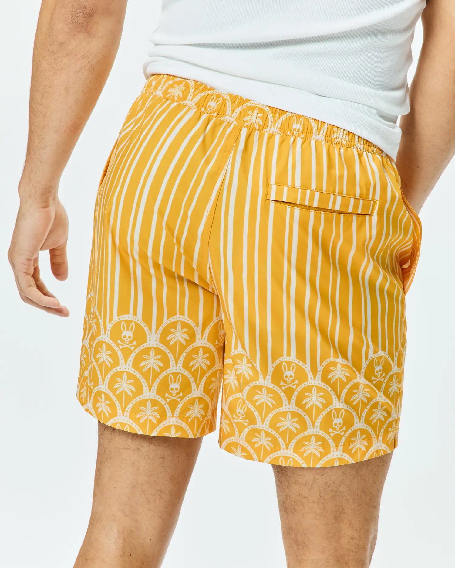 Mens Brad Swim Trunk in mustard yellow with white vertical stripes, a scalloped hem featuring palm trees and small Psycho Bunny skull logos, and an elastic waistband.