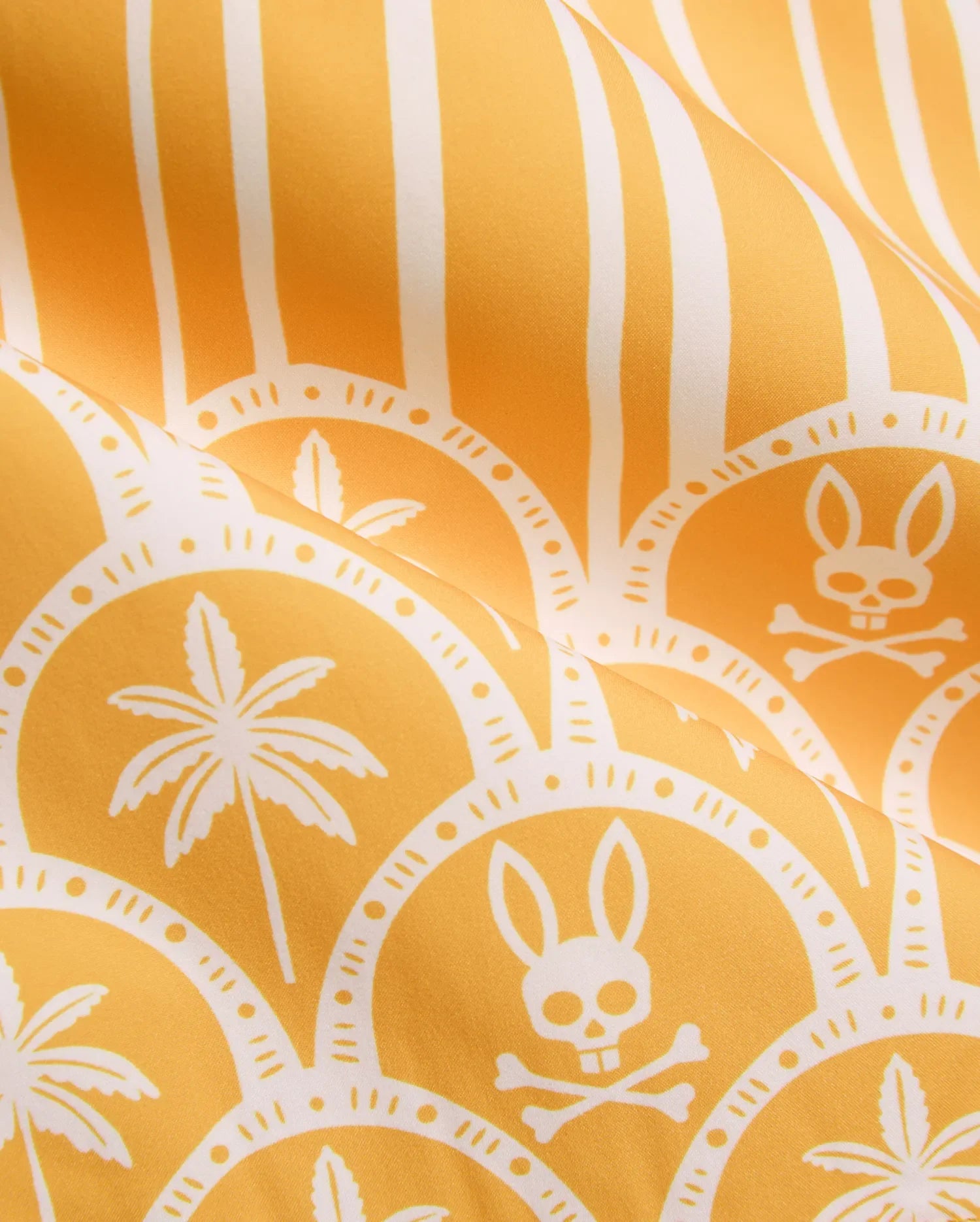 Vibrant yellow Mens Brad Swim Trunk with white vertical stripes, scalloped pattern, palm tree graphics, and repeated Psycho Bunny skull and crossbones logos on smooth quick-dry fabric.