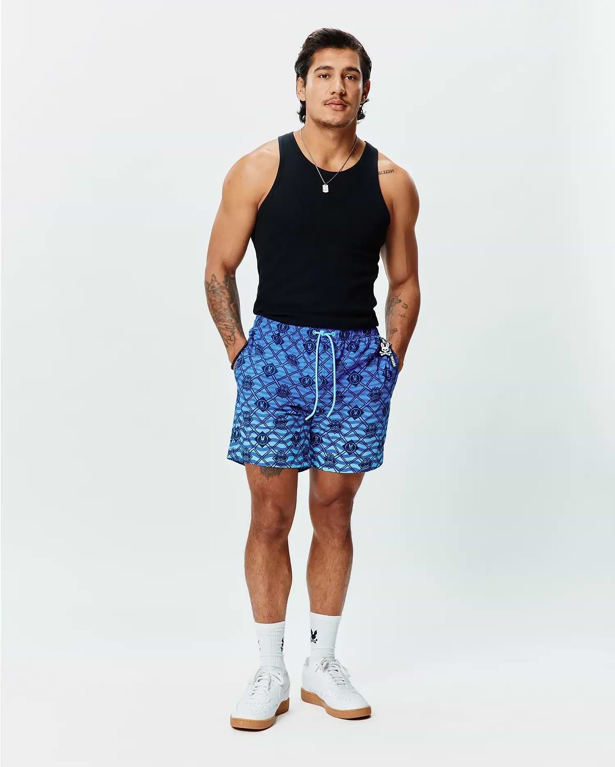 Mens Tobias Gradient Swim Trunk, a blue gradient all-over diamond pattern featuring repeating Psycho Bunny skull logos, with a white drawstring and small logo tag on the right pocket. Relaxed fit. (4)