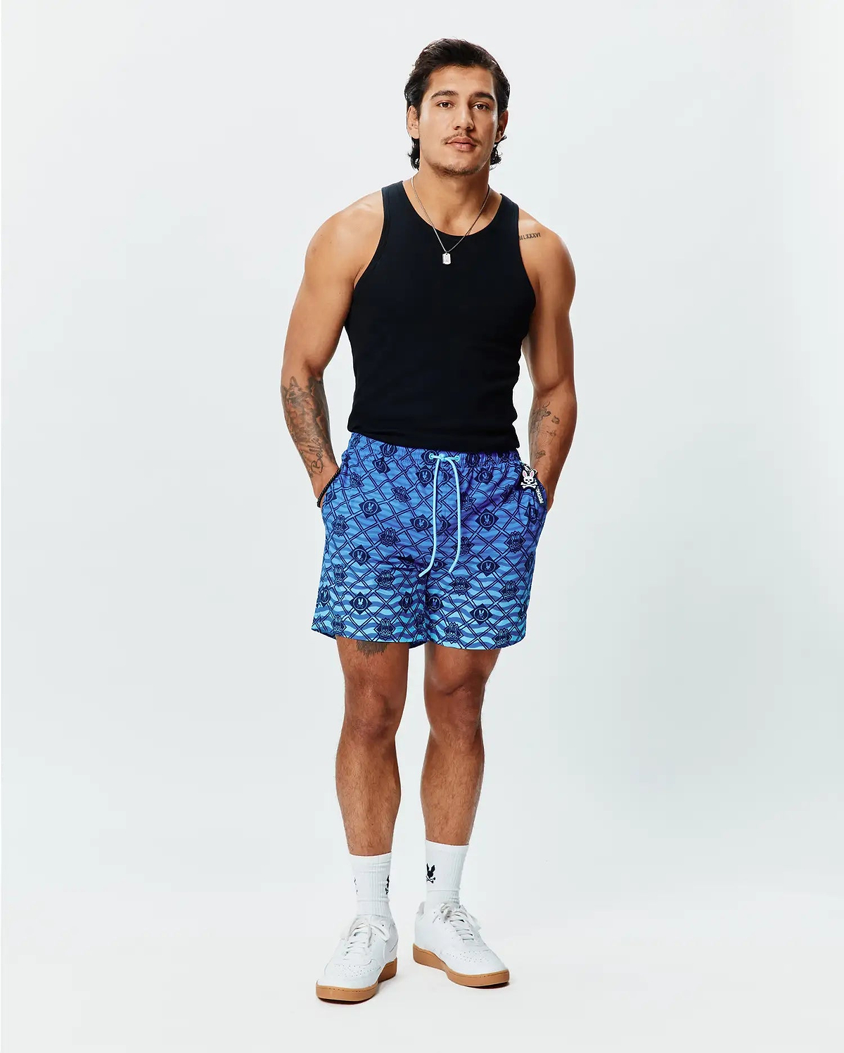 Mens Tobias Gradient Swim Trunk, a blue gradient all-over diamond pattern featuring repeating Psycho Bunny skull logos, with a white drawstring and small logo tag on the right pocket. Relaxed fit. (4)