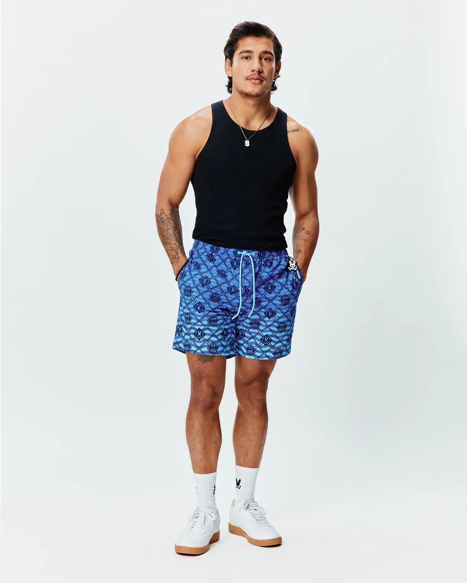 Mens Tobias Gradient Swim Trunk, a blue gradient all-over diamond pattern featuring repeating Psycho Bunny skull logos, with a white drawstring and small logo tag on the right pocket. Relaxed fit. (4)