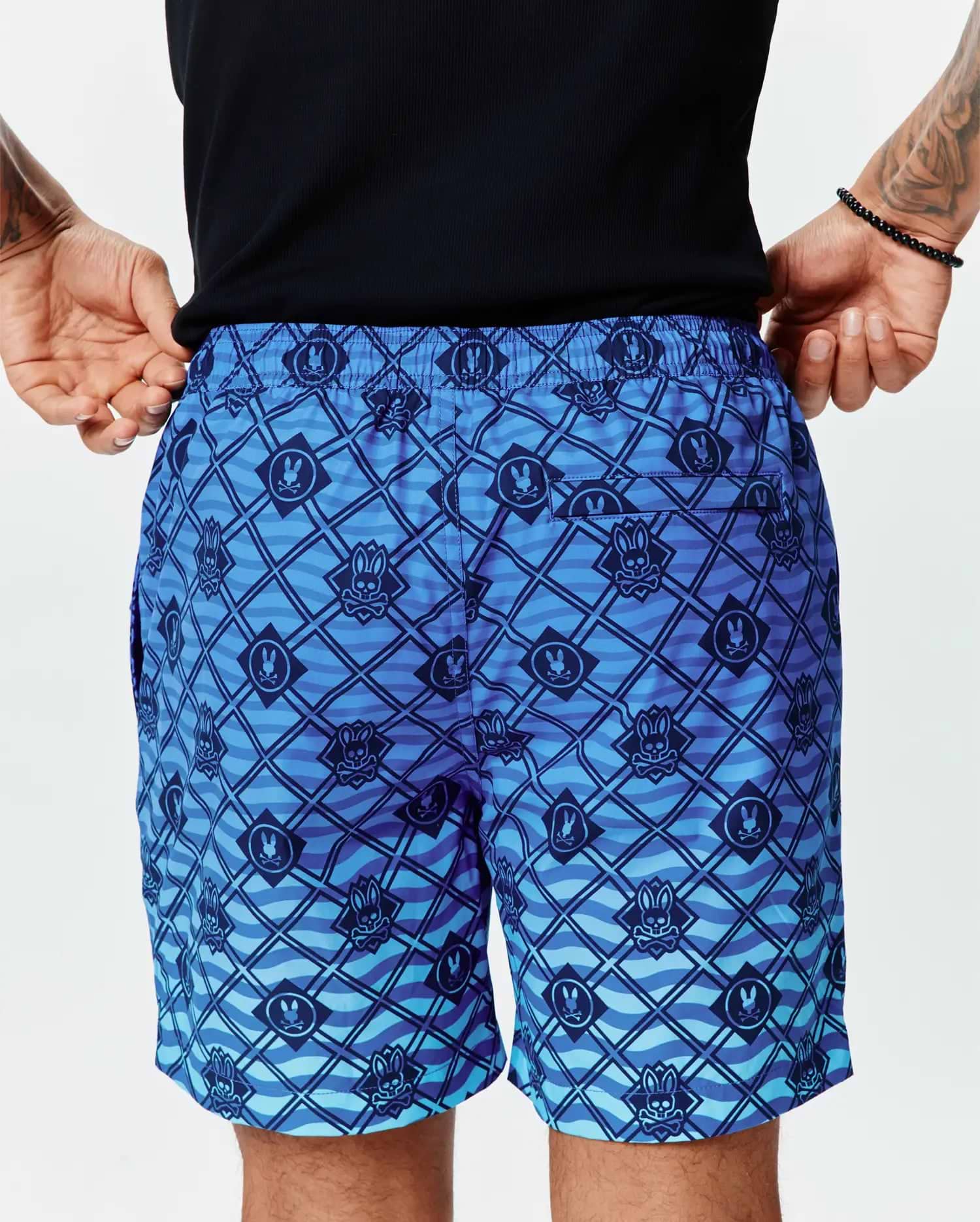 Mens Tobias Gradient Swim Trunk in a blue gradient with an all-over dark blue Psycho Bunny skull logo and diagonal grid pattern over a wavy background on smooth, relaxed-fit quick-dry fabric. (3)