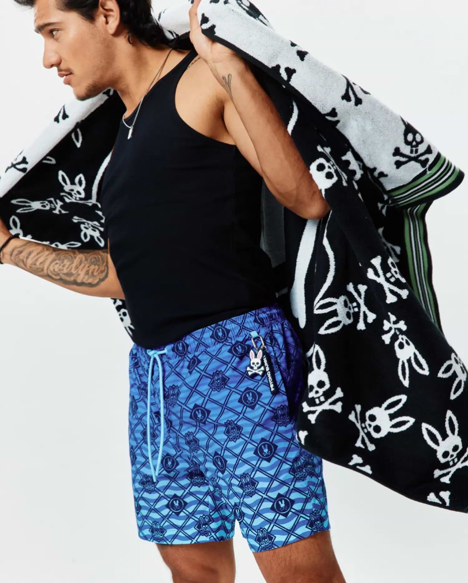 Mens Tobias Gradient Swim Trunk featuring an all-over blue geometric wave pattern with integrated small Psycho Bunny skull logos, light blue drawstring, and a Psycho Bunny keychain. (2)