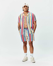 Mens Hubert Swim Trunk in vibrant multi-color vertical stripes (pink, orange, yellow, blue, red), featuring a relaxed fit, textured quick-dry fabric, and a small embroidered Psycho Bunny skull logo on the left leg.