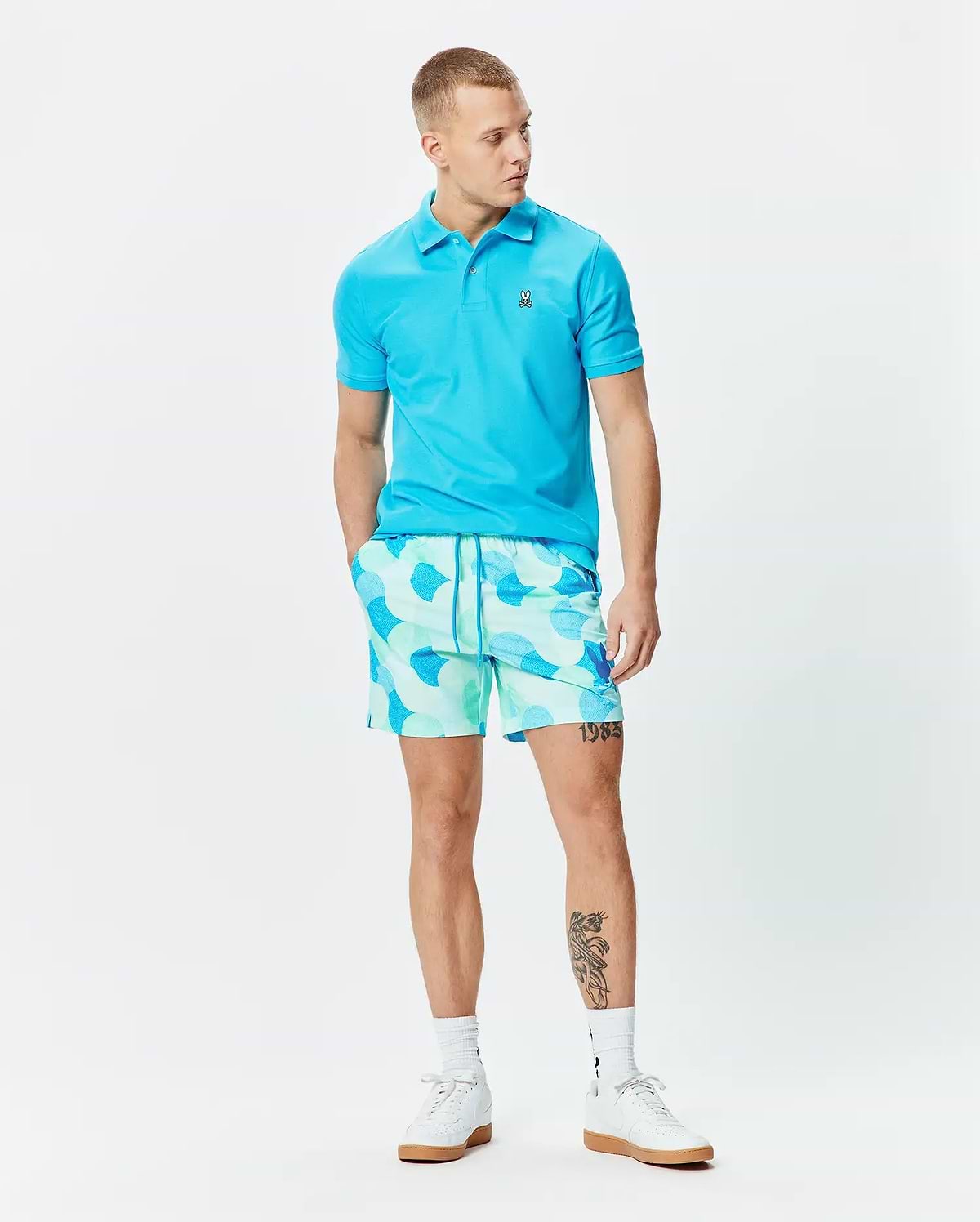 Bright blue pique polo with embroidered Psycho Bunny skull logo on chest, paired with Mens Ethan Swim Trunk 6 featuring a mint green and blue abstract pattern and drawstring waist. (4)