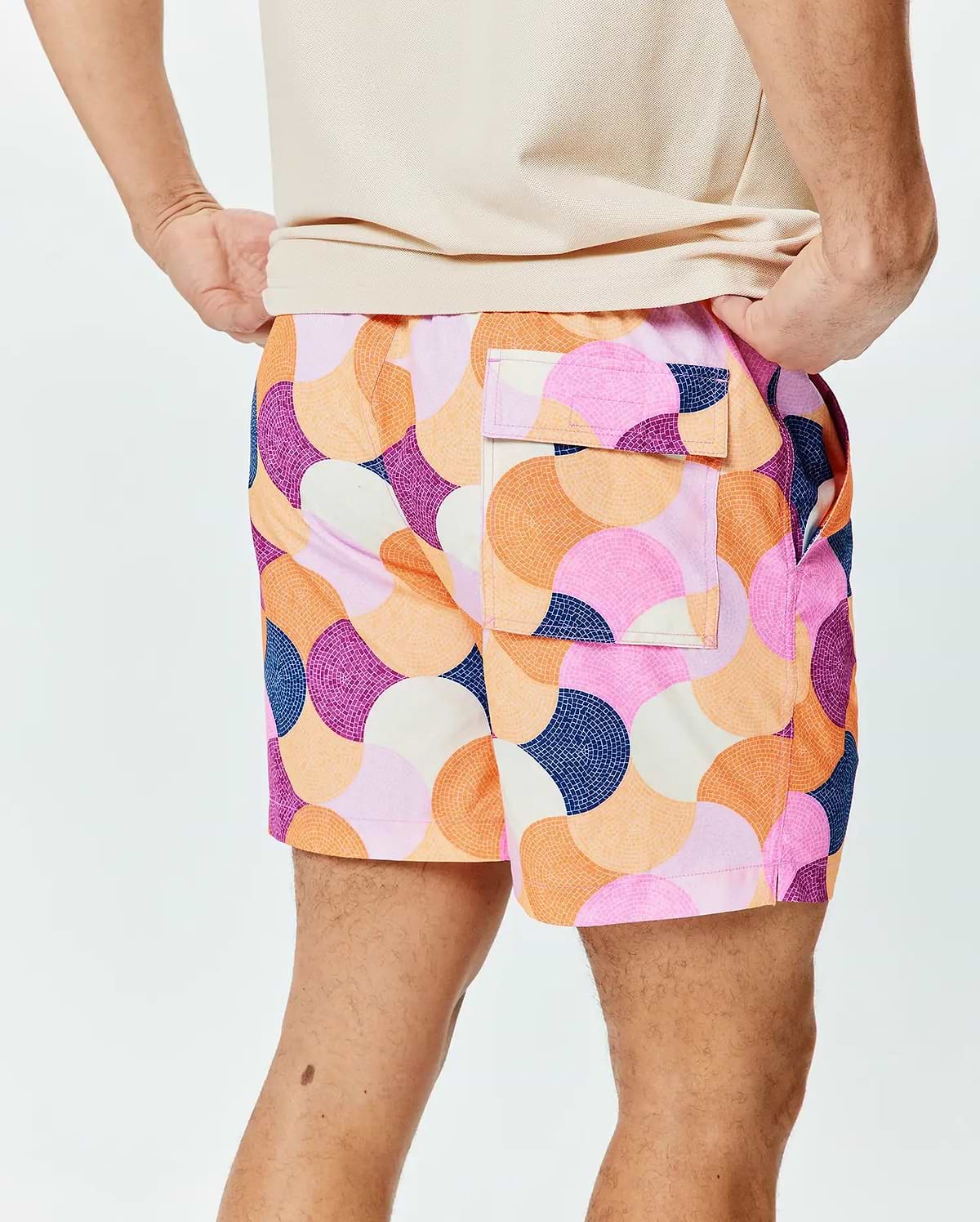 Mens Ethan Swim Trunk 6, a vibrant, relaxed-fit swim trunk with smooth fabric. It features a bold mosaic-style circular pattern in pink, orange, purple, navy, and cream, with side and back flap pockets. (2)