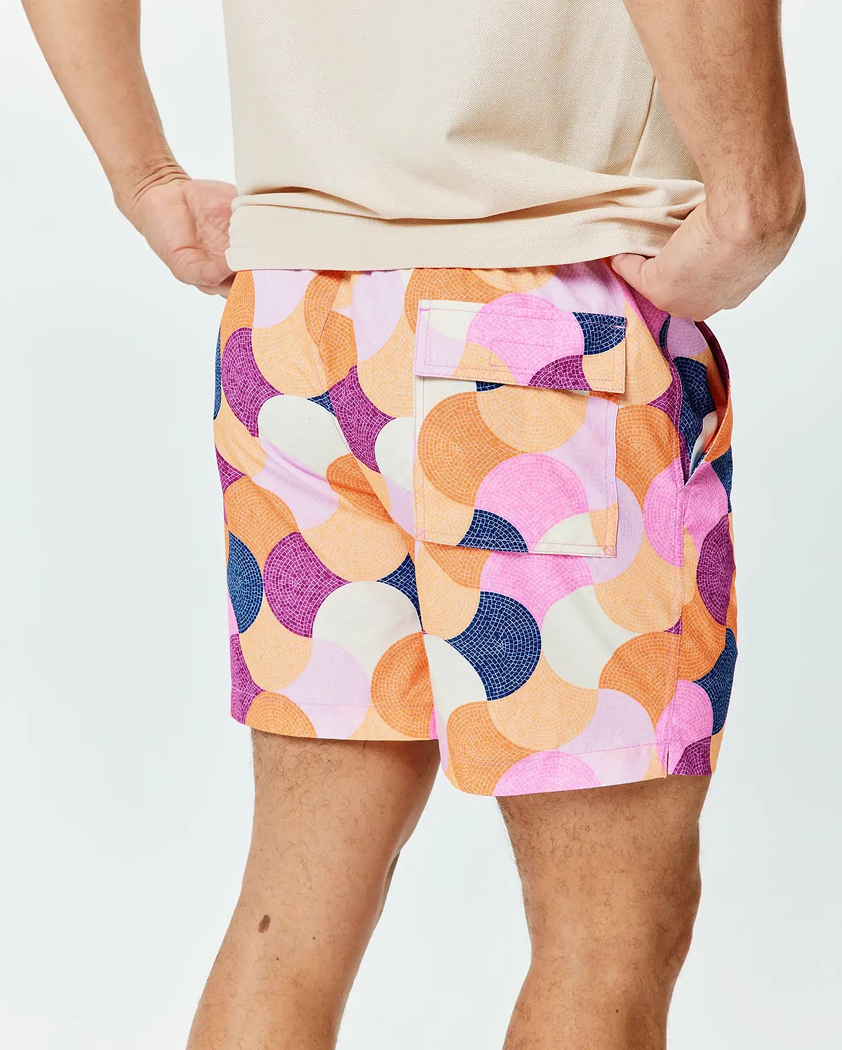 Mens Ethan Swim Trunk 6, a vibrant, relaxed-fit swim trunk with smooth fabric. It features a bold mosaic-style circular pattern in pink, orange, purple, navy, and cream, with side and back flap pockets. (2)