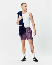 Mens Frank Swim Trunk 6, a vibrant purple and lilac all-over geometric pattern with integrated Psycho Bunny skull logos, featuring a relaxed fit and black drawstring.