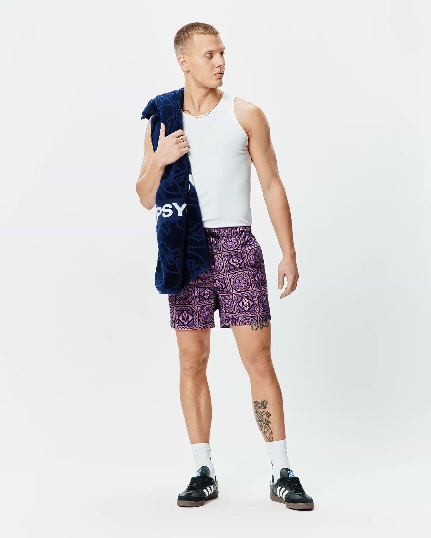 Mens Frank Swim Trunk 6, a vibrant purple and lilac all-over geometric pattern with integrated Psycho Bunny skull logos, featuring a relaxed fit and black drawstring.