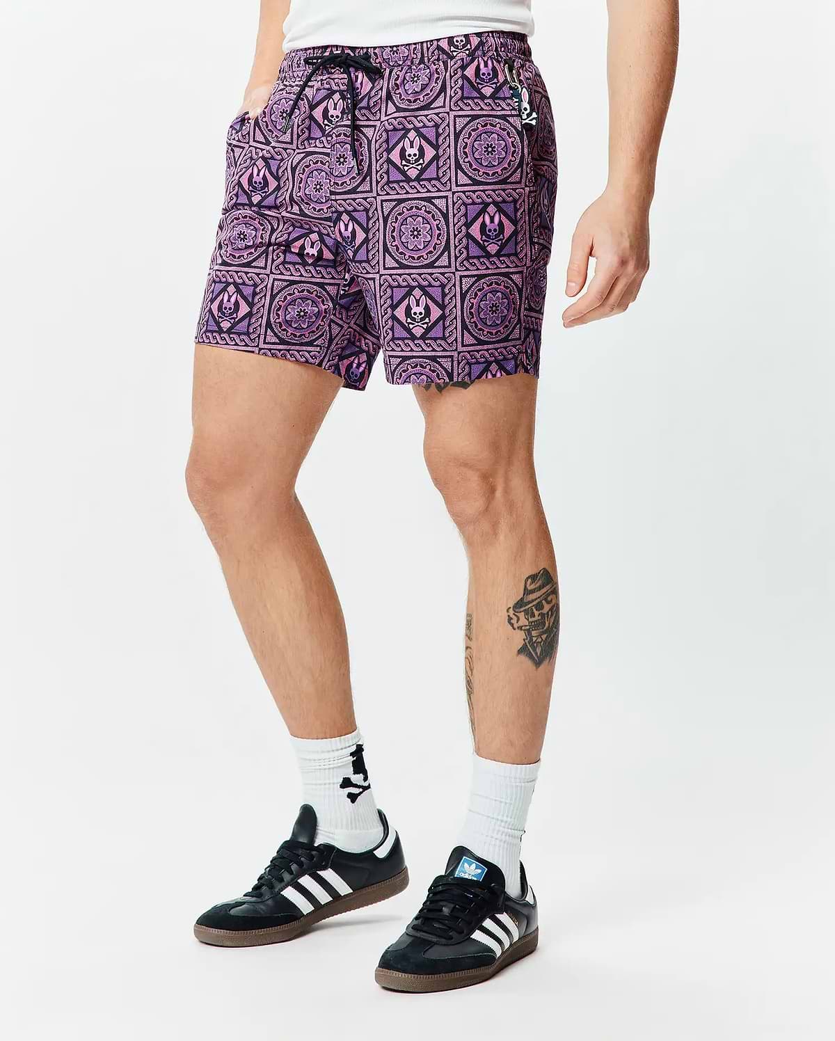 Mens Frank Swim Trunk 6, purple and pink geometric pattern with black outlines, featuring repeating Psycho Bunny skull logos and circular motifs on smooth swim fabric.