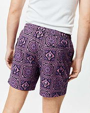 Mens Frank Swim Trunk 6, vibrant purple and black mosaic print swim trunks featuring repeating pink Psycho Bunny skull logos and intricate floral patterns, classic fit, smooth quick-dry fabric.