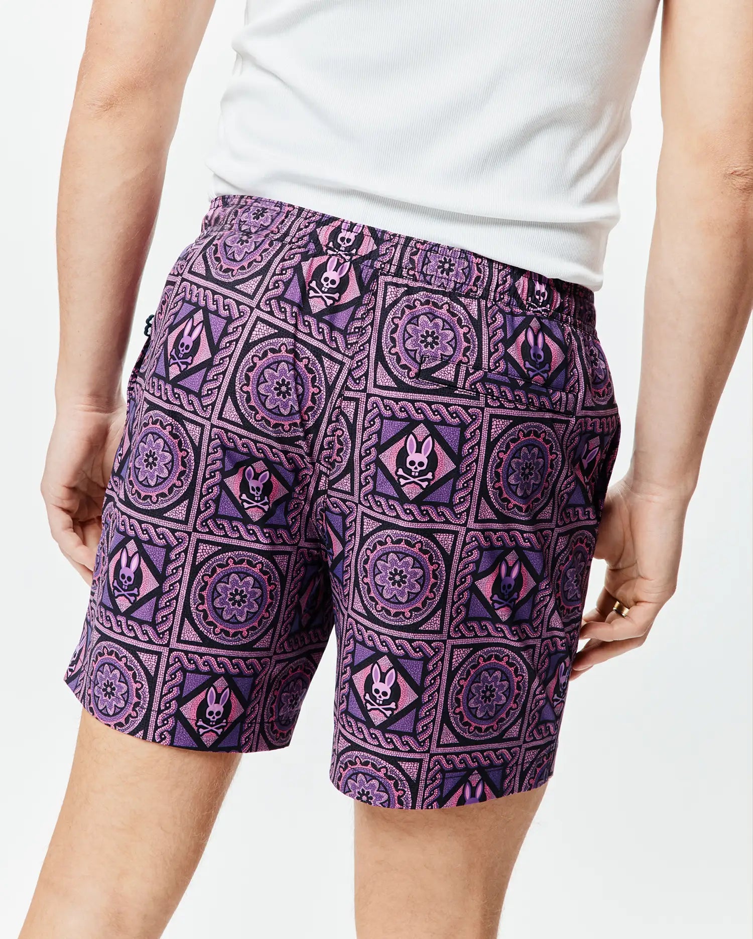 Mens Frank Swim Trunk 6, vibrant purple and black mosaic print swim trunks featuring repeating pink Psycho Bunny skull logos and intricate floral patterns, classic fit, smooth quick-dry fabric.