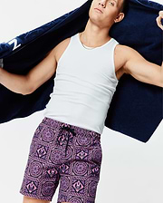 Mens Frank Swim Trunk 6 in vibrant purple and pink, featuring an all-over geometric and floral tile pattern with repeated small Psycho Bunny skull logos, classic fit, smooth fabric, and black drawstring.