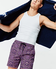 Mens Frank Swim Trunk 6 in vibrant purple and pink, featuring an all-over geometric and floral tile pattern with repeated small Psycho Bunny skull logos, classic fit, smooth fabric, and black drawstring.