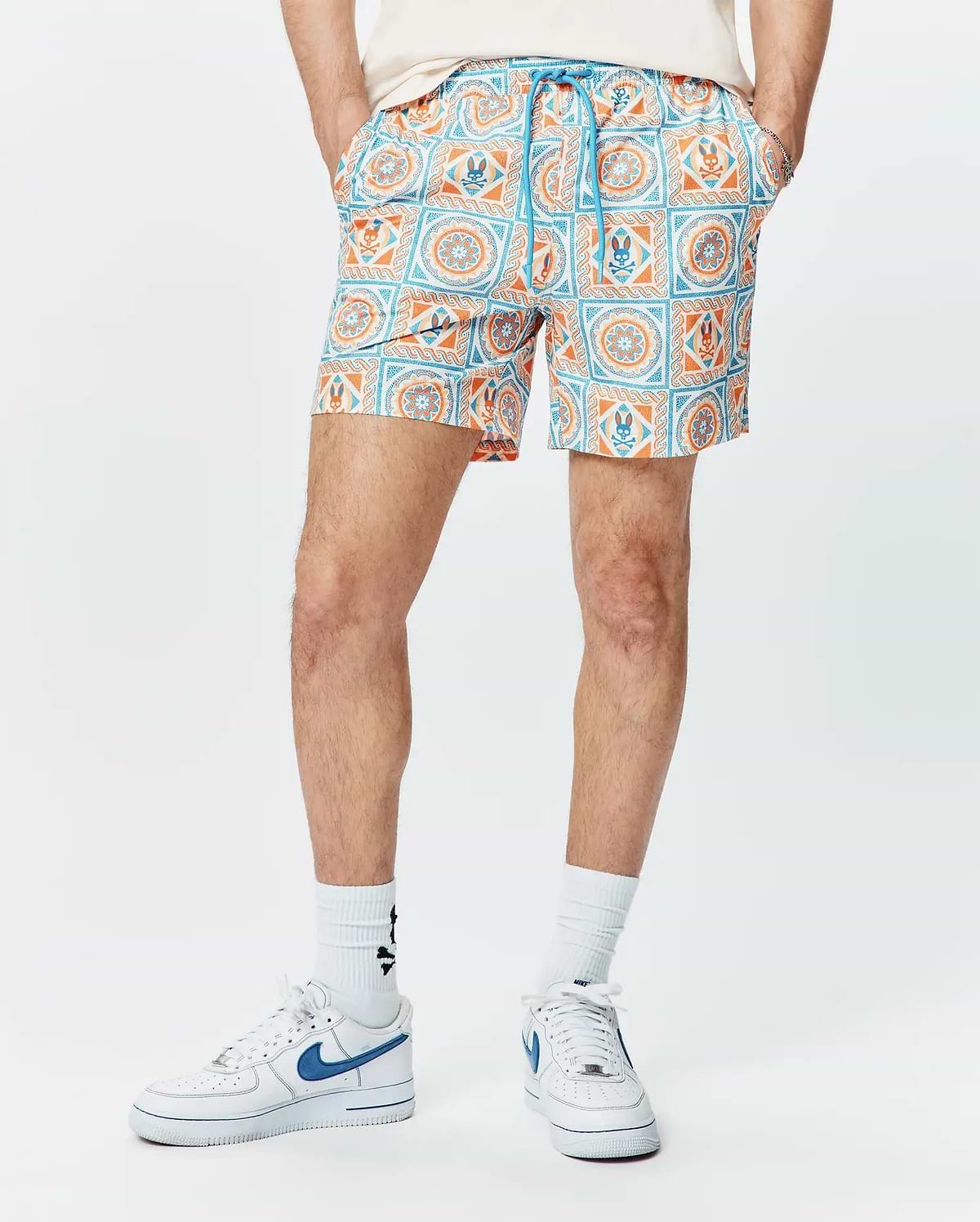 Mens Frank Swim Trunk 6, a classic fit swim trunk with a vibrant white, orange, and blue tiled geometric pattern featuring the iconic Psycho Bunny skull logo and a blue drawstring.