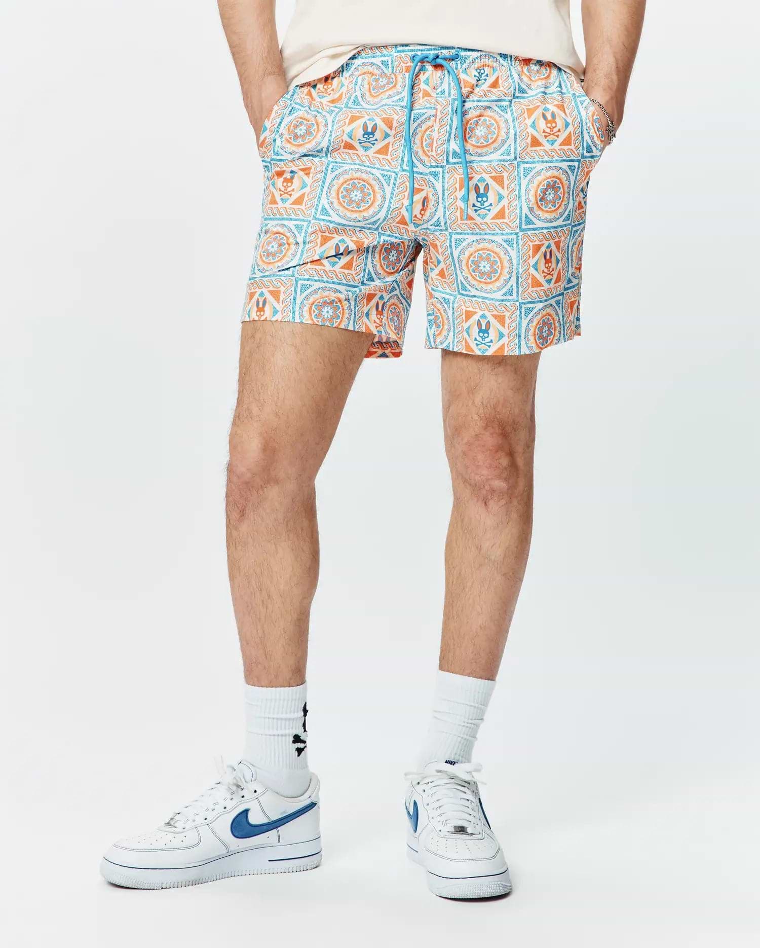Mens Frank Swim Trunk 6, a classic fit swim trunk with a vibrant white, orange, and blue tiled geometric pattern featuring the iconic Psycho Bunny skull logo and a blue drawstring.
