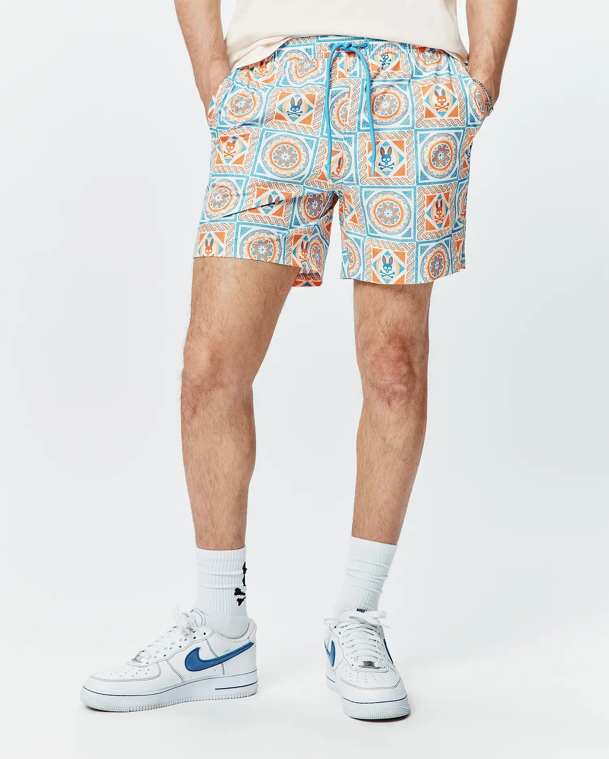 Mens Frank Swim Trunk 6, a classic fit swim trunk with a vibrant white, orange, and blue tiled geometric pattern featuring the iconic Psycho Bunny skull logo and a blue drawstring.