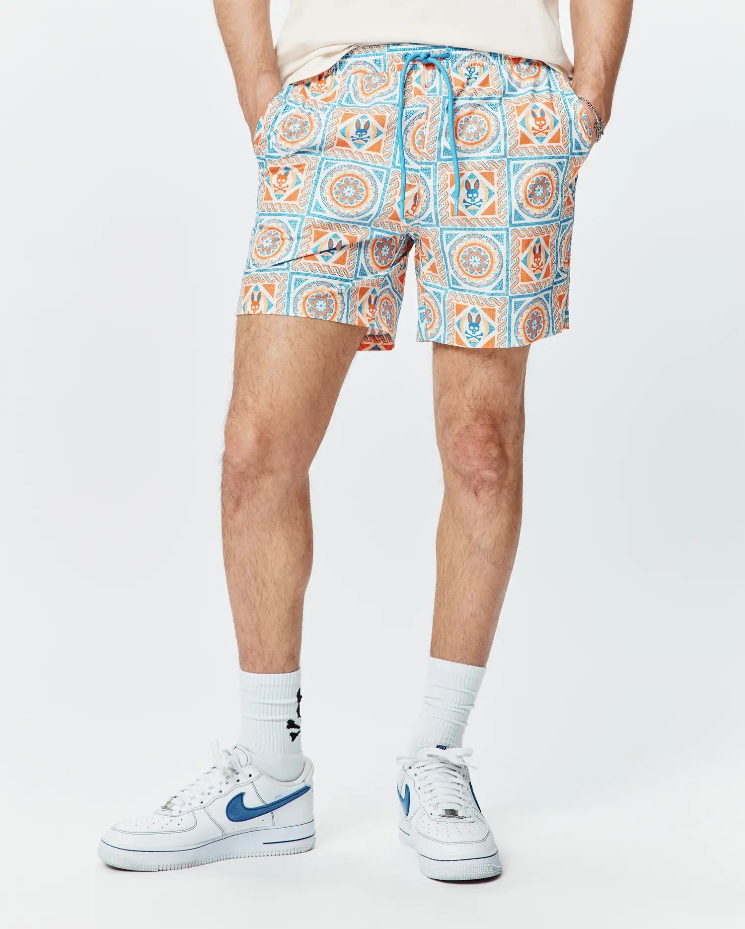 Mens Frank Swim Trunk 6, a classic fit swim trunk with a vibrant white, orange, and blue tiled geometric pattern featuring the iconic Psycho Bunny skull logo and a blue drawstring.