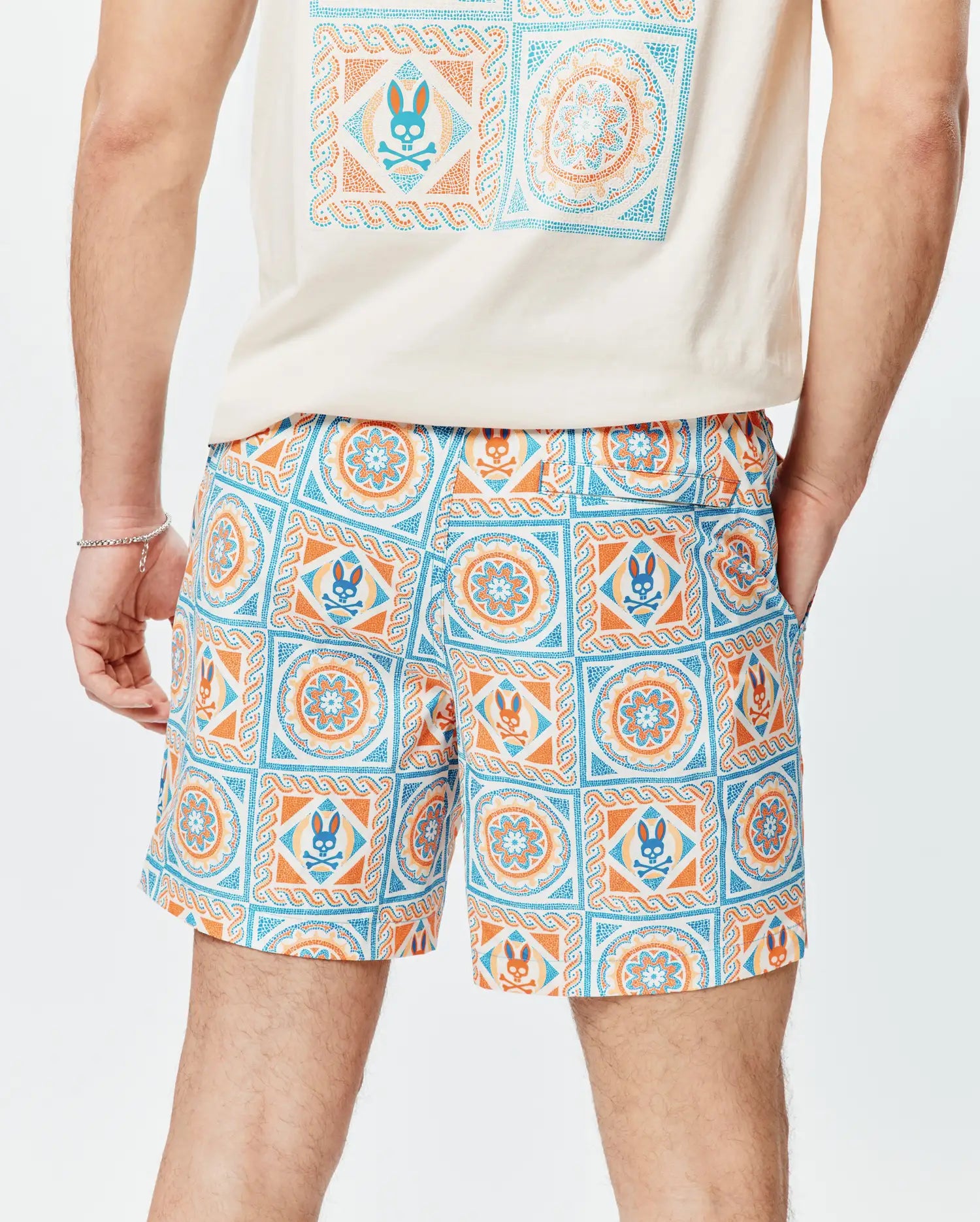 Mens Frank Swim Trunk 6, a classic fit, white swim trunk with a vibrant blue and orange mosaic tile pattern, featuring the iconic Psycho Bunny skull logo integrated throughout the print. Smooth fabric.