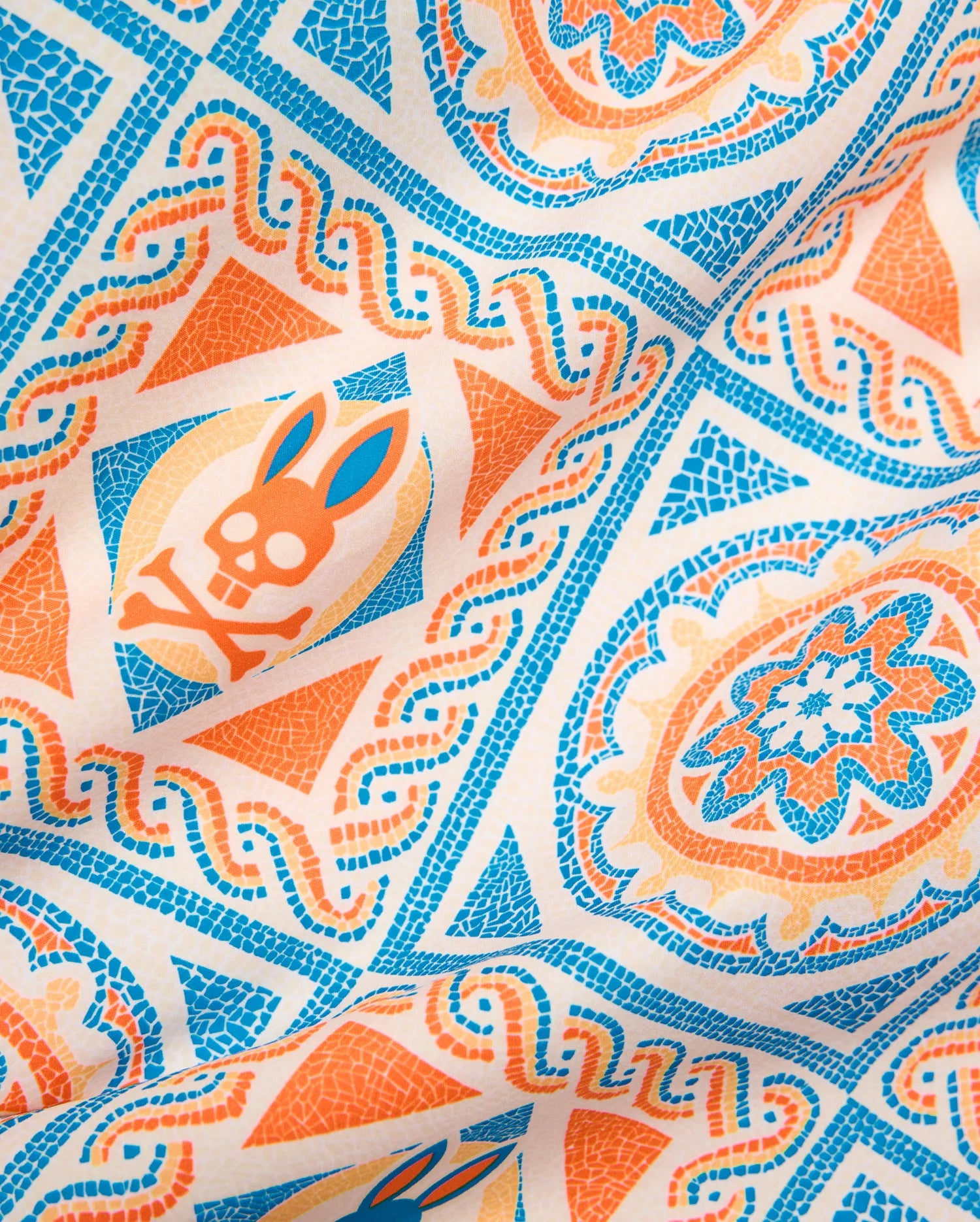 Mens Frank Swim Trunk 6, a smooth woven fabric with an off-white base, vibrant blue, orange, and peach mosaic-style all-over pattern featuring the iconic Psycho Bunny skull logo.