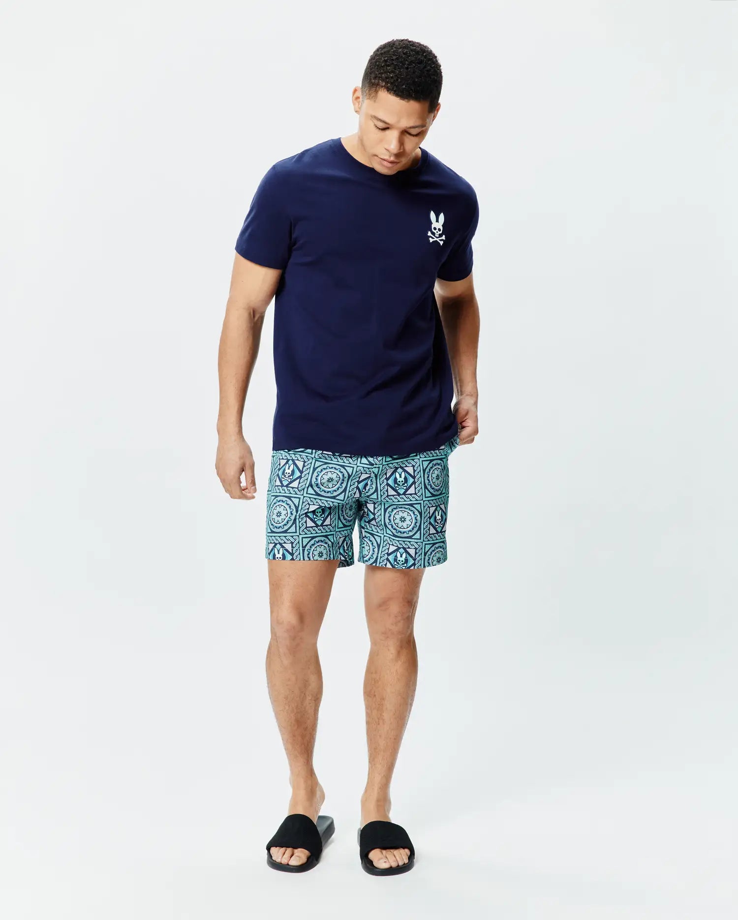 Navy blue classic fit jersey t-shirt with small white Psycho Bunny skull logo on left chest, paired with Mens Frank Swim Trunk 6 featuring an all-over teal and blue geometric pattern with integrated bunny skulls.