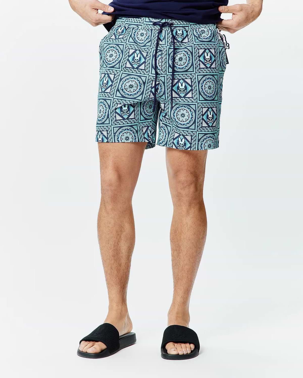 Mens Frank Swim Trunk 6 in teal and navy with an all-over geometric pattern featuring repeated white Psycho Bunny skull logos, classic fit, smooth quick-dry fabric, and navy drawstring.
