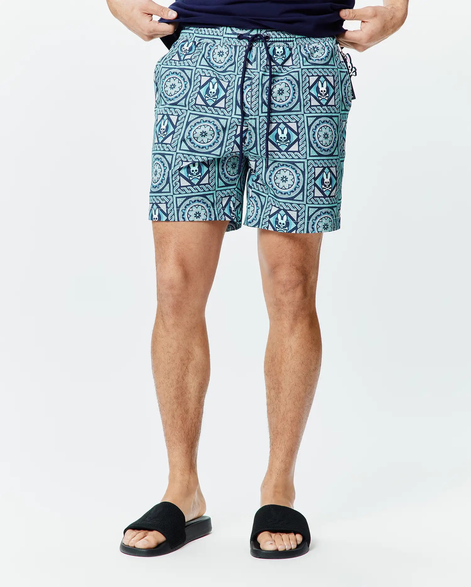 Mens Frank Swim Trunk 6 in teal and navy with an all-over geometric pattern featuring repeated white Psycho Bunny skull logos, classic fit, smooth quick-dry fabric, and navy drawstring.
