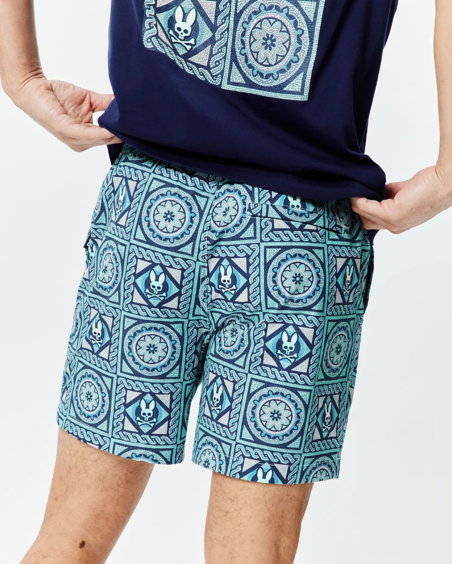 Mens Frank Swim Trunk 6, a classic fit swim trunk in a vibrant blue and teal mosaic pattern, intricately featuring the iconic Psycho Bunny skull logo and floral designs throughout the smooth fabric.
