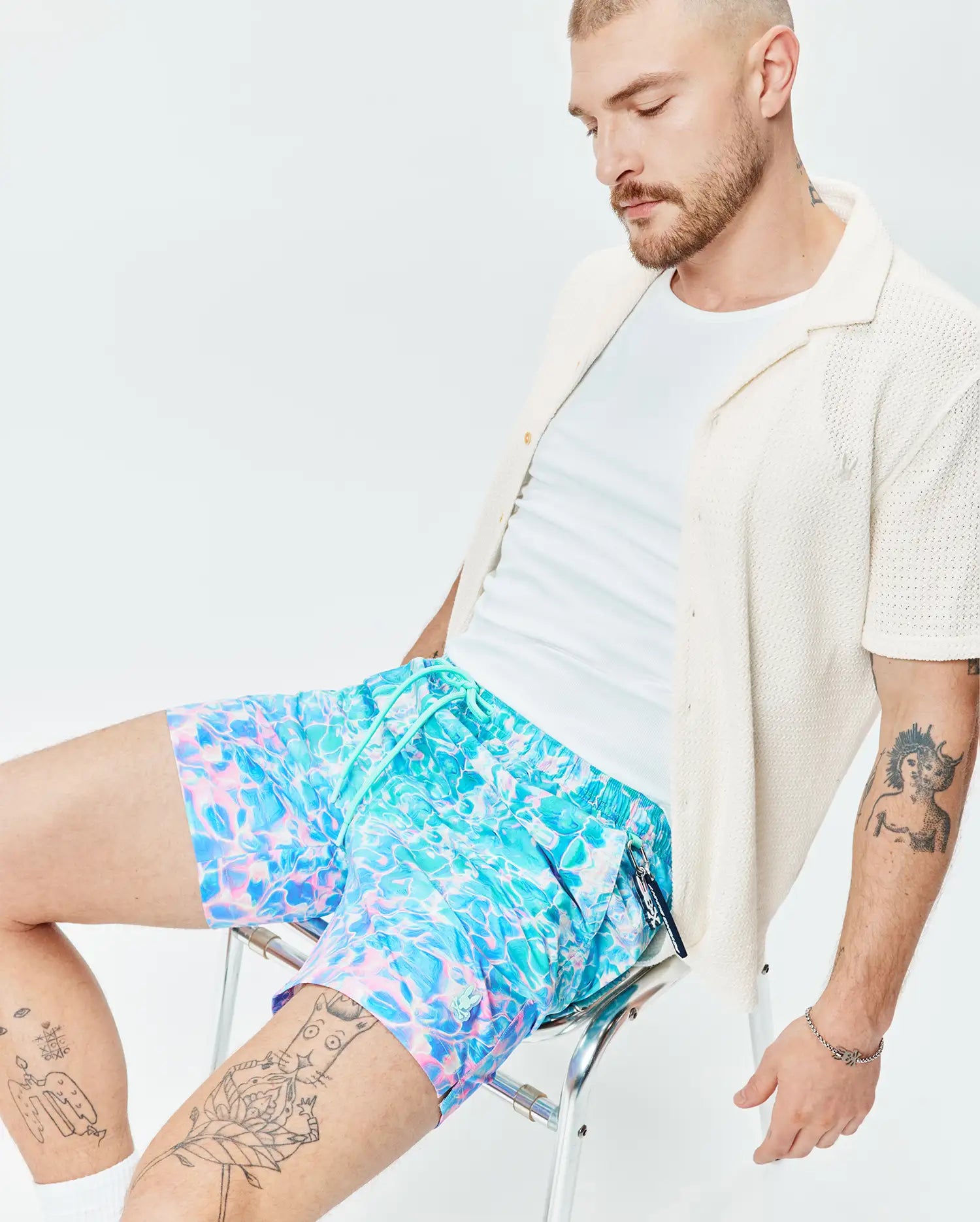 Mens Dayton Swim Trunk 6, featuring a vibrant blue and pink abstract water ripple print, elastic waistband with turquoise drawstring, and a small Psycho Bunny skull logo patch on the left leg. (3)