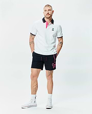 White pique polo with black and pink striped collar, embroidered Psycho Bunny logo, and black Mens Duncan Bunny Print Swim Trunk featuring a large pink bunny skull graphic and pink drawstring.