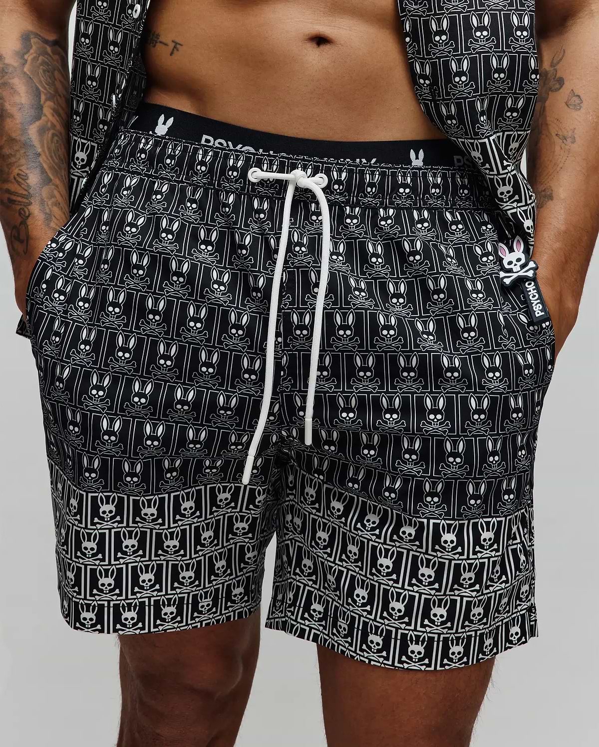 Mens Keon All Over Bunny Swim Trunk, black with a white repeating bunny skull pattern, white drawstring, branded waistband, and a small rubberized Psycho Bunny tag with a pink bunny skull.