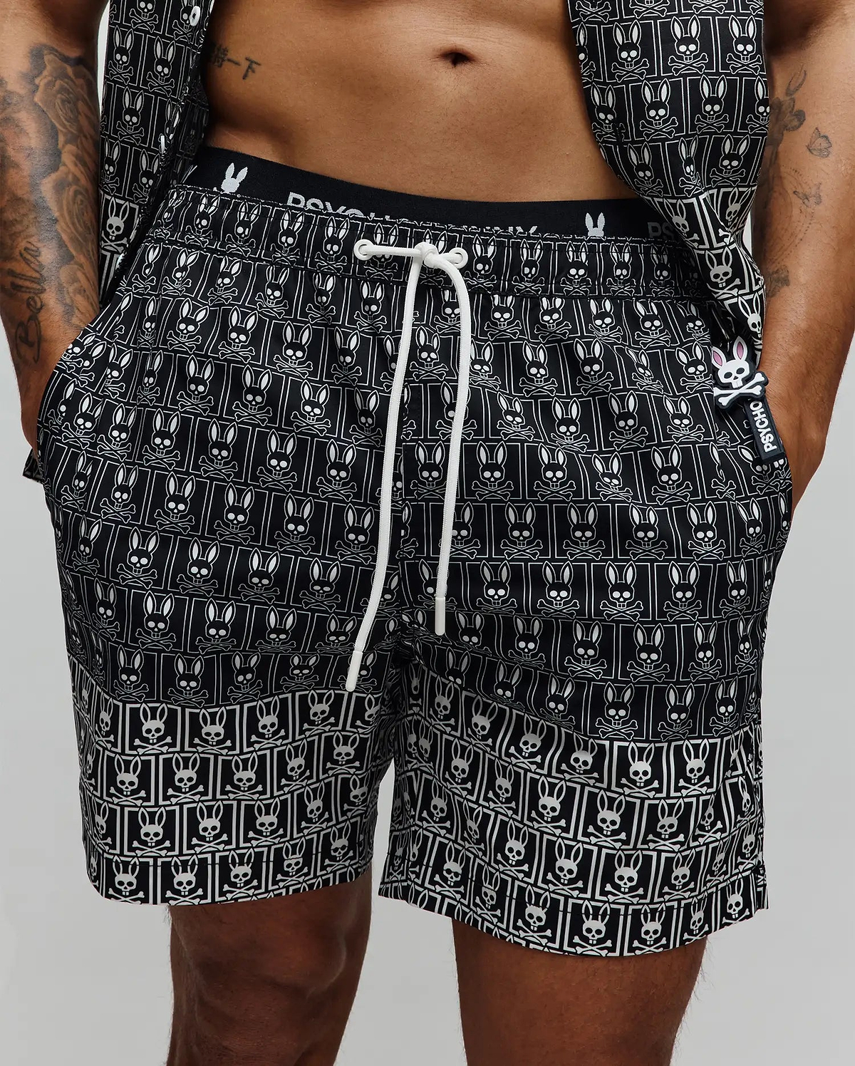 Mens Keon All Over Bunny Swim Trunk, black with a white repeating bunny skull pattern, white drawstring, branded waistband, and a small rubberized Psycho Bunny tag with a pink bunny skull.