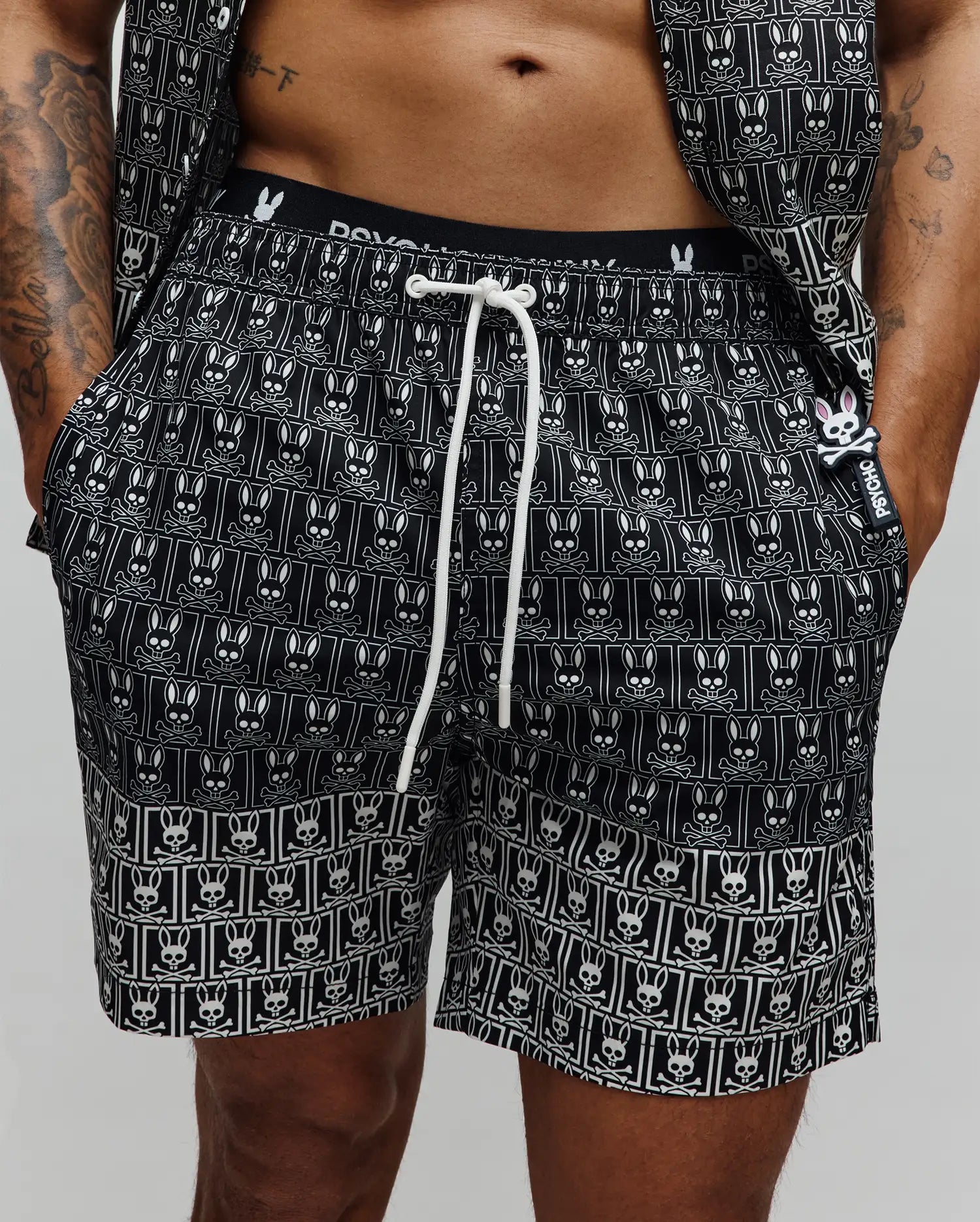 Mens Keon All Over Bunny Swim Trunk, black with a white repeating bunny skull pattern, white drawstring, branded waistband, and a small rubberized Psycho Bunny tag with a pink bunny skull.
