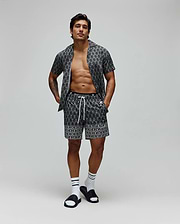 Mens Keon All Over Bunny Swim Trunk and matching short-sleeve shirt in black with a white all-over Psycho Bunny skull logo print, featuring a relaxed fit, smooth fabric, and white drawstring.