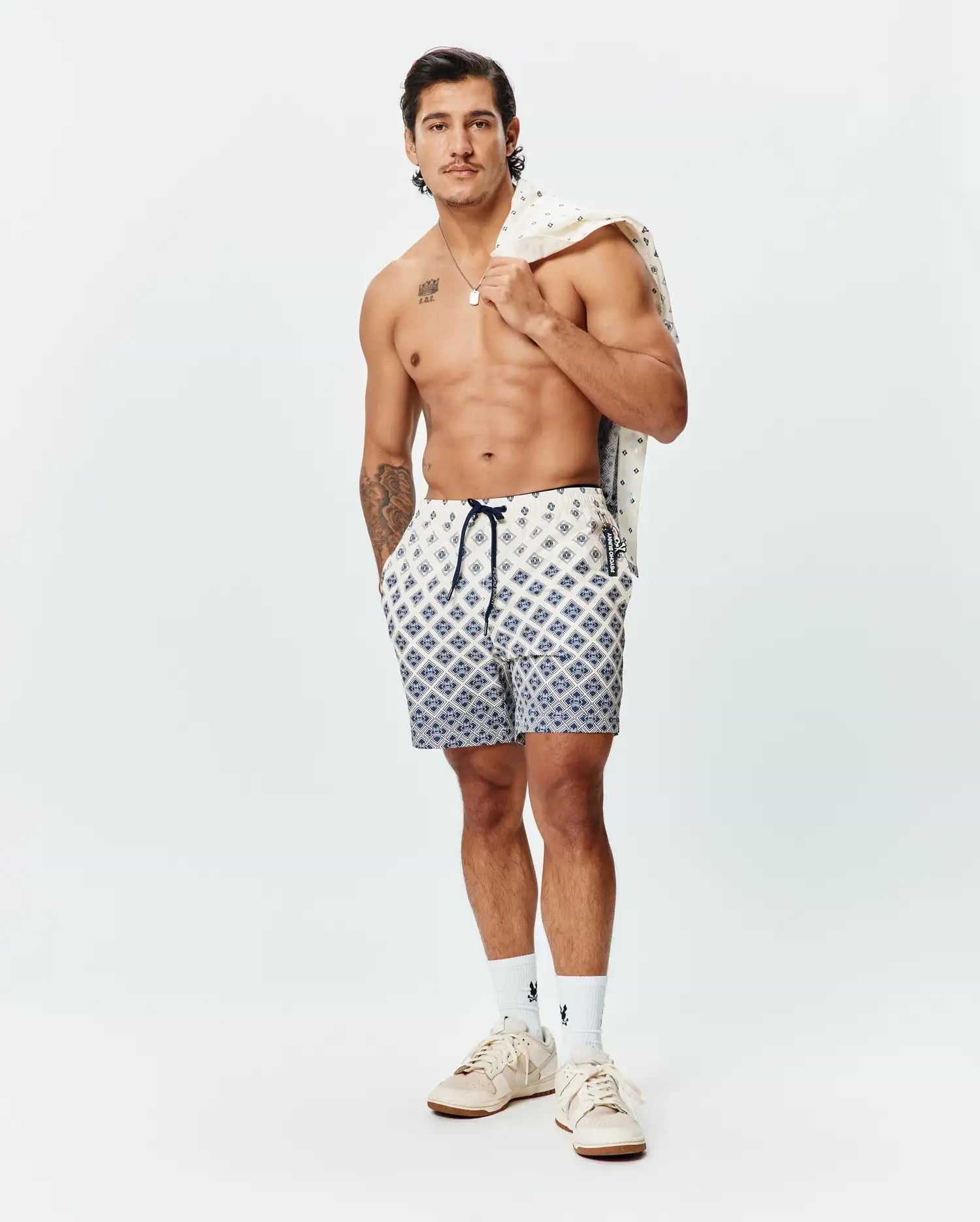 Mens Tobias Swim Trunk in cream with a navy blue geometric pattern, featuring a navy drawstring, small Psycho Bunny skull logo on the left leg, and a branded side tag.