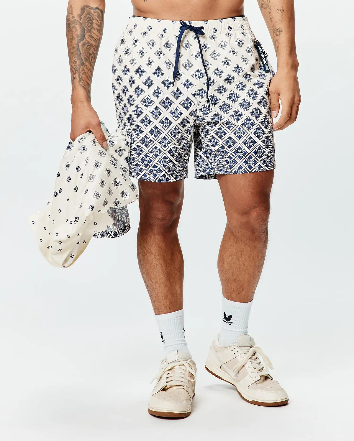 Mens Tobias Swim Trunk in cream with a navy geometric diamond pattern featuring integrated Psycho Bunny skull logos, a navy drawstring, and a branded side tag.