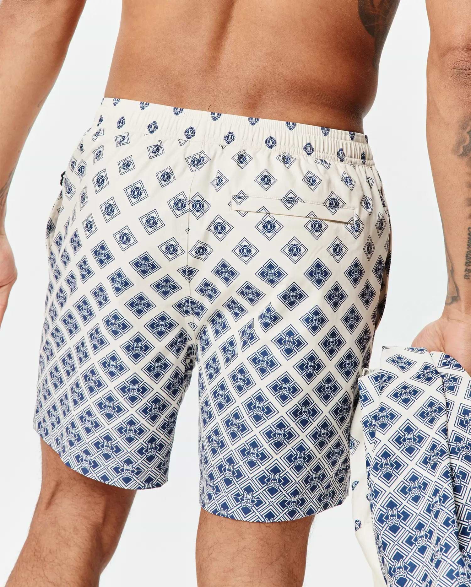 Mens Tobias Swim Trunk in cream with a navy blue all-over geometric pattern featuring the small Psycho Bunny skull logo, classic fit, smooth quick-dry fabric, and a back pocket.